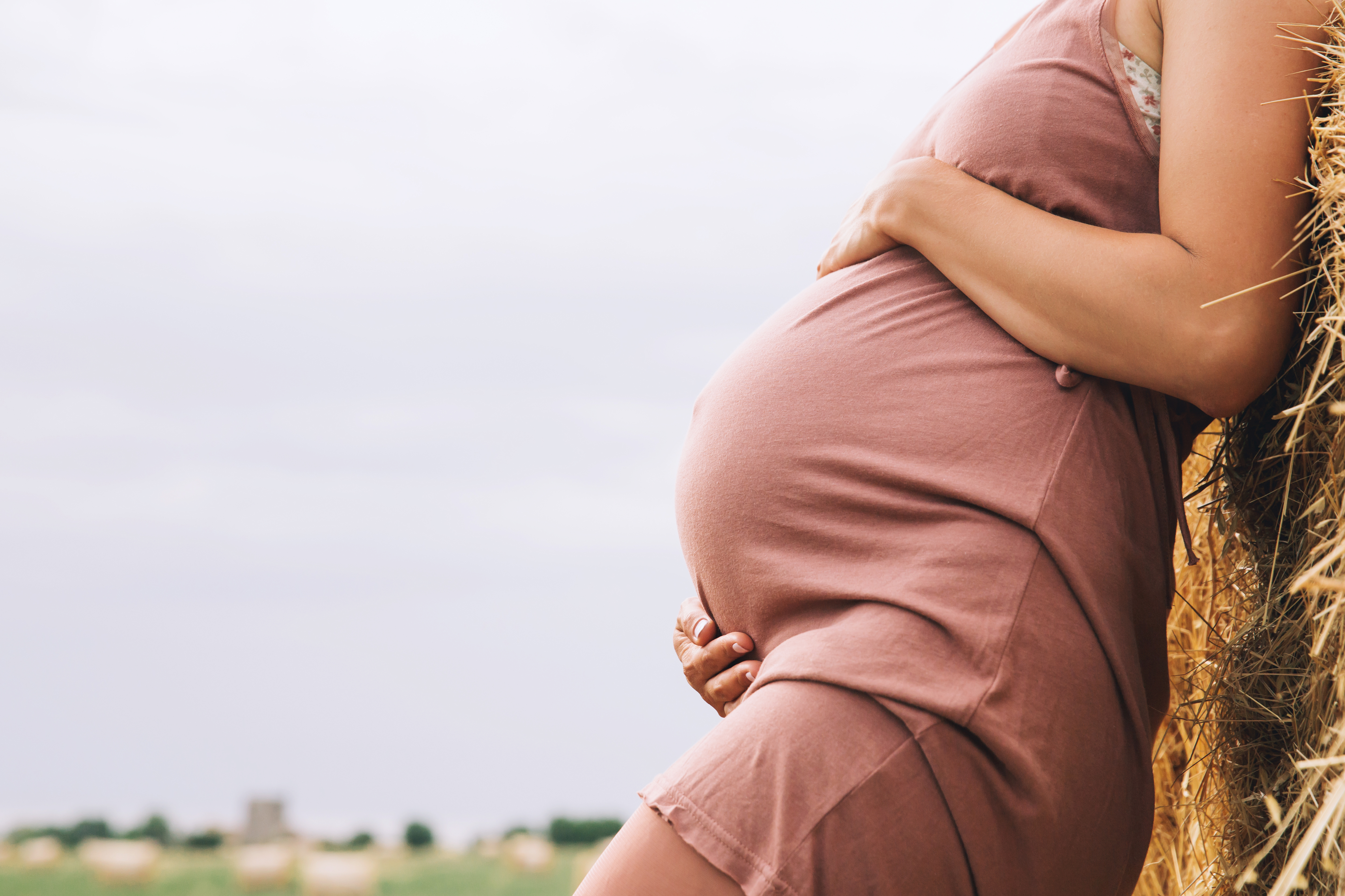 A pregnant woman cradling her belly outdoors
